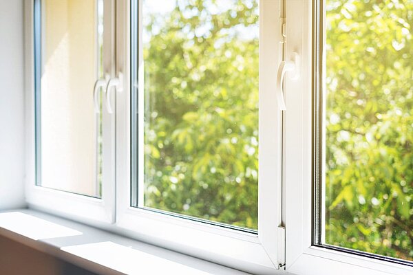 Geöffnetes weißes Kunststofffenster in Innenansicht mit Blick auf grünen Garten und natürlichem Lichteinfall