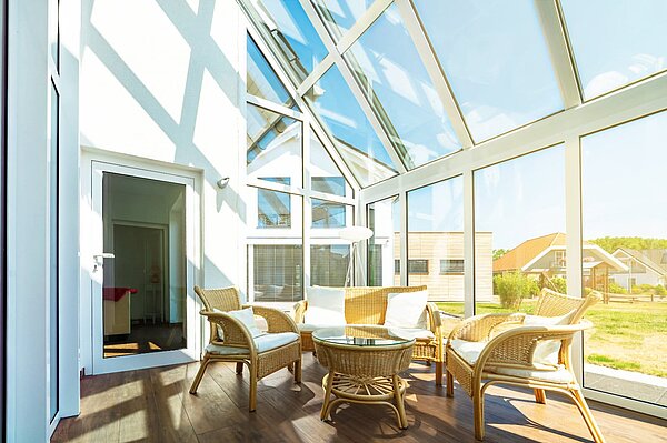 Lichtdurchfluteter Wintergarten mit vollständiger Glas-Konstruktion, Rattanmöbeln und Blick ins Grüne