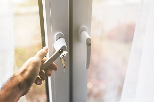Hand öffnet modernes Fenster mit abschließbarem Griff und Schlüssel, Fenstersicherheit im Wohnbereich