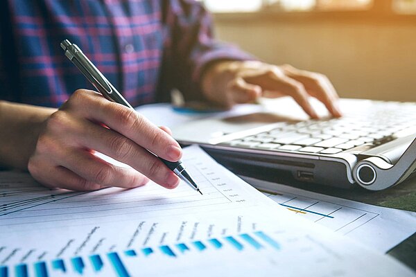 Person bei Finanzplanung am Schreibtisch mit Taschenrechner, Stift und Diagrammen zu Sanierungskosten